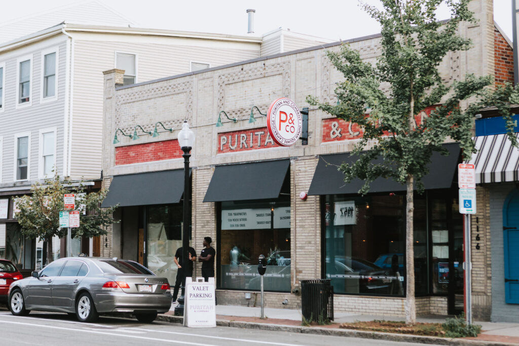 The exterior of Puritan & Co. A gray building with a red banner.