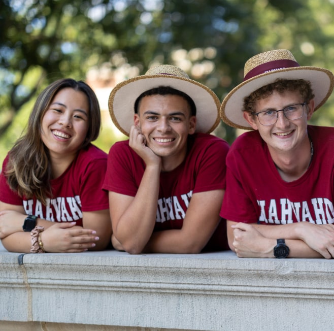 Three friends in red Harvard shirts pose for a photo in Harvard Square, Cambridge Massachusetts