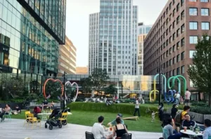 People relaxing and socializing in a landscaped urban park plaza surrounded by modern office buildings.